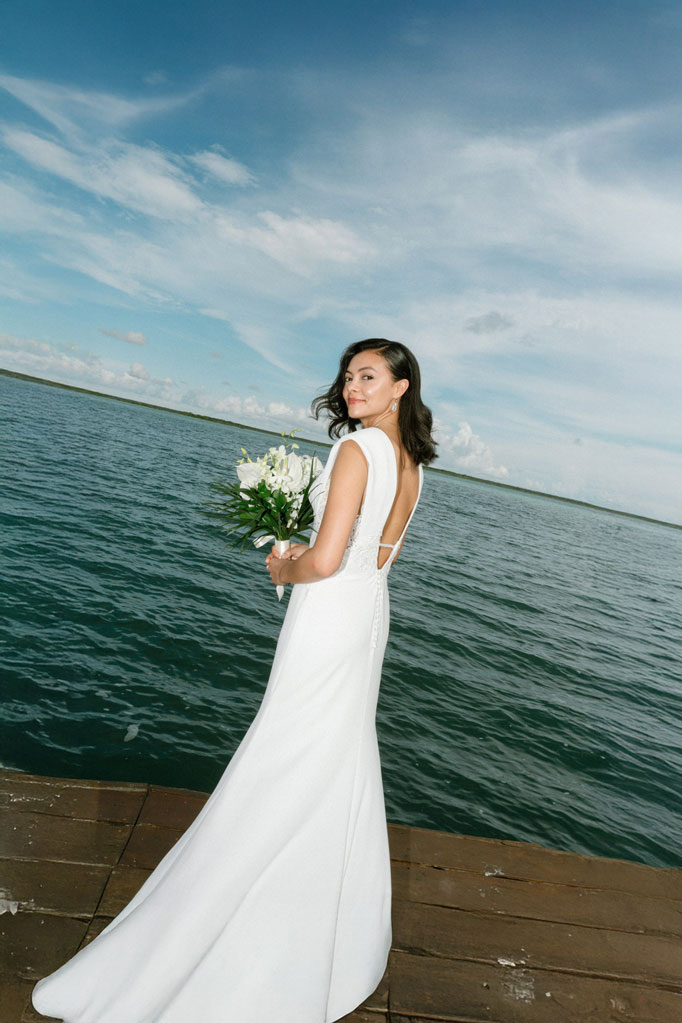 Bride in a white wedding dress holding a bouquet by the ocean for a destination wedding in Los Cabos.